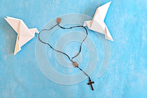 White dove origami carrying rosary or scapular in sky blue background.