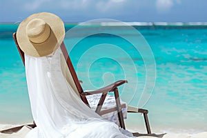 white dress on beach chair with straw hat, turquoise sea backdrop