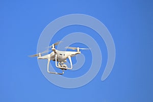 White drone, with a camera flies against blue cloudless sky. Quadrocopter, unmanned aerial vehicle in flight
