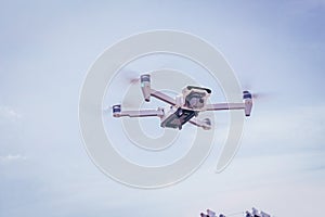 White drone hovering in a bright blue sky. Drone copter flying with digital camera
