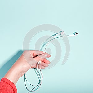 White earphones in female hand on pastel background, copy space. Modern technology flat lay with cordless earphones in woman hand