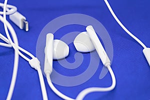 White earpods on blue background with the cable, music listening devices concept - Image