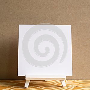 White easel with blank canvas on wooden desk