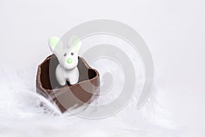 White Easter Bunny in a cracked chocolate egg in a white soft feather nest, close-up, copy space. Easter marzipan rabbit
