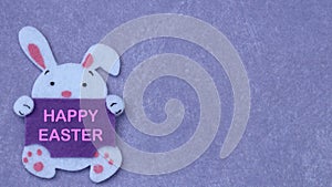 White easter bunny made from felt laying on purple background with copy space