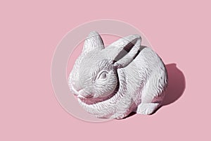 White Easter bunny rabbit with trendy shadow sitting on pink background. Easter symbol