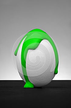 White easter egg with liquid color splash on the grey background