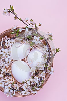 White easter eggs in a basket with flowers on a pink background. Vertical photograph. Top view