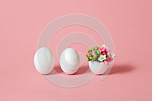 White Easter eggs with beautiful spring flowers on pink background