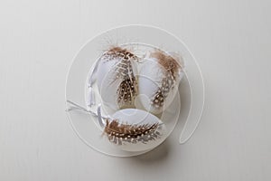 White easter eggs are decorated with a feather. Eggs are on a white table