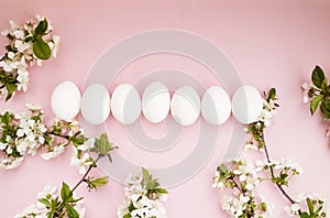 White easter eggs, white spring flowers on a pink background. Happy Easter. Place for text. Top view. Flat lay