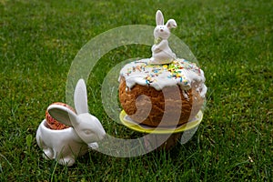 white Easter rabbit standing on home-baked easter cakes with icing on a plate on green background