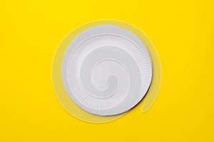 White eco-friendly paper plate on yellow colored paper background. top view. mock-up