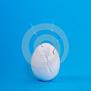 White egg close-up in cracks with needles on a blue background. The concept of the threat of weakened immunity in