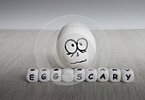 White egg with frightened face on white wooden background