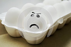 White egg with painted angry face in the tray