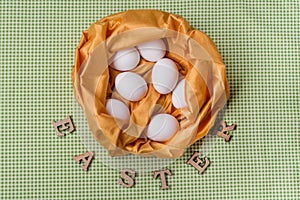 White eggs in an abstract nest of yellow textures, green background of tablecloths in the kitchen