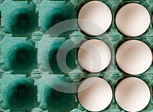 White eggs arranged together to the right side of a green egg carton with empty spaces on the left side.