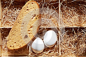 White eggs and bread in a wooden box with a straw