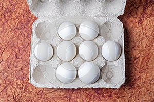 White eggs in a carton box on a brown textured paper background