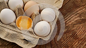 White eggs carton and cracked egg half with yolk top view on wooden background