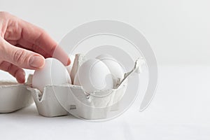 White eggs in a eggbox with a hand standing on a white table