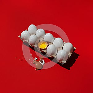 White eggs and one broken dark brown egg in a common tray on red background. Tolerance, inequality, racial