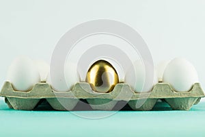 White eggs in a paper box and one unique golden egg inside them on white background. Leadership, genius, uniqueness concept. photo