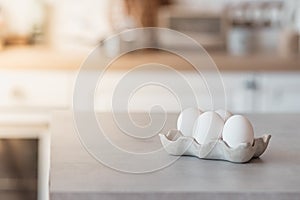 White eggs in a stand lie on a gray concrete table in the kitchen. Sunlight in the corner, Easter card.