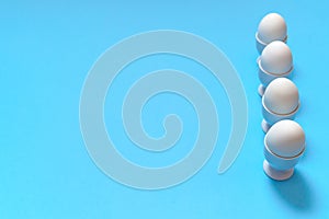 White eggs standing on egg cup isolated on blue background, copy space. Row of boiled eggs in stand. Healthy food concept. Easter