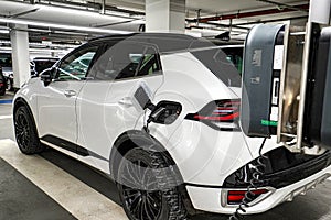 A white electric car is charging in an underground parking lot. The concept of ecological energy systems