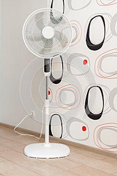 A white electric fan stands in a spacious room and cools the air.