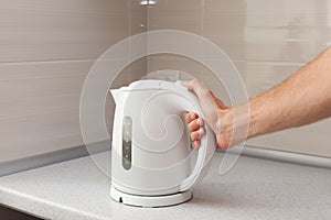White electric Kettle in hand on the background of the kitchen