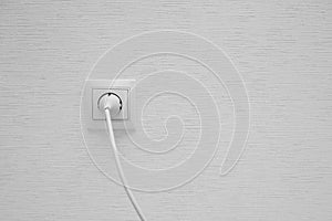 White electrical plug in the electric socket on a wall.