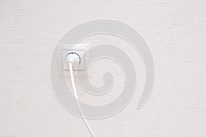 White electrical plug in the electric socket on a wall.