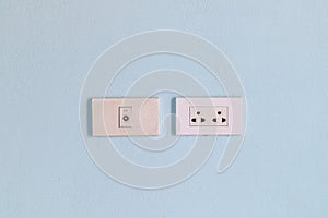 The white electrical plug socket on a blue concrete wall.