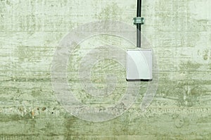 White electrical power outlet with cover cap and black cable attached on grunge concrete wall.