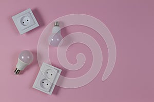 White electrical power sockets, light lamp bulbs on light pink background. Top view