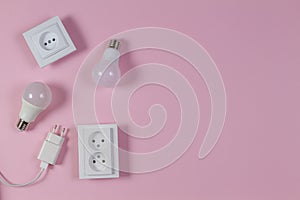 White electrical power sockets, power plugs, light lamp bulbs on light pink background. Top view