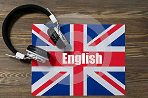 White electronic headphones lying on the flag of Great Britain with the text-English. Close-up, brown wooden background