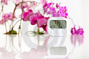 White electronic hygrometer on white table with orchids on the background. Fahrenheit mode