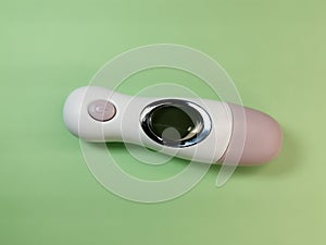 White electronic non-contact thermometer for measuring body temperature in children and adults on a light-green background