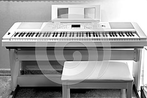 White electronic piano on stand with chair near wall - monochrome