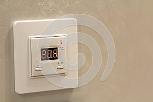 White electronic programmable digital thermostat on light wall copy space background. Climate control, comfortable home