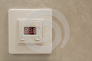 White electronic programmable digital thermostat on light wall copy space background. Climate control, comfortable home