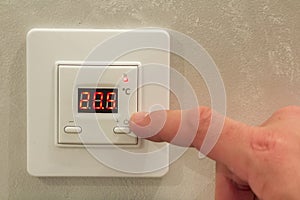 White electronic programmable digital thermostat on light wall copy space background. Climate control, comfortable home