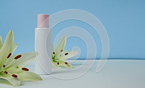 White empty cosmetic bottle with cream with pink cap, moisturizing lotion or shampoo framed with fresh lily flowers on a light