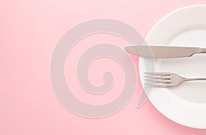 White empty plate with fork and knife on a pink table