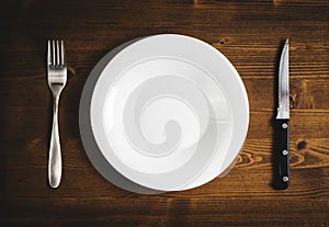 White empty plate with a fork and knife on a wooden table