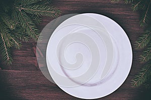 White empty plate with a green branch of spruce on a wooden surf